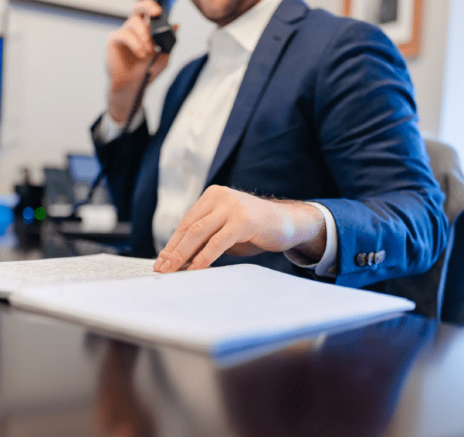 Businessman in blue suit making notes on document while holding phone in office setting